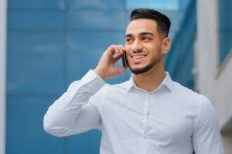 Hispanic indian bearded businessman with mobile phone at street smiling Arabian businessman manager